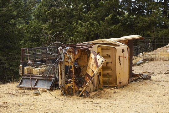 Overturned rusted vehicle in a wooded area, surrounded by twisted metal parts, wrecked vehicle, Crete, Greek Islands, Greece