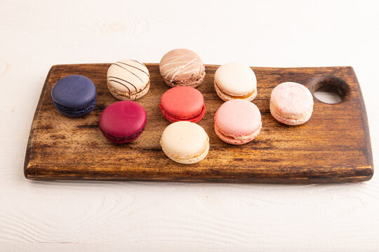 Macarons colourful cookies dessert on brown wooden cutting board on white wooden, side view, close up
