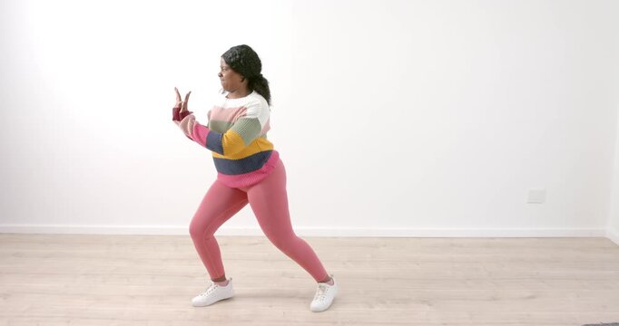 African American woman dancing energetically in colorful sweater on wooden floor