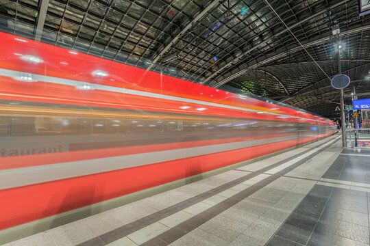 View of a high-speed train passing through a modern railway station with motion blur and steel roof structure in Berlin, Berlin, Germany.