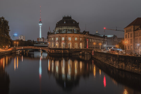 View of the illuminated Bode Museum at night with its reflection in the Spree river and the Berlin TV Tower in the background in Berlin, Berlin, Germany.