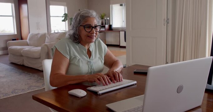 Senior woman typing on keyboard at home, smiling and enjoying technology