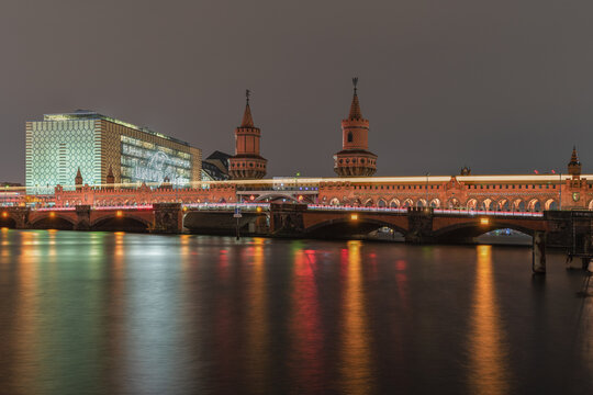 View of the illuminated Oberbaum Bridge at night with light trails from a passing train and reflections on the Spree river in Berlin, Berlin, Germany.