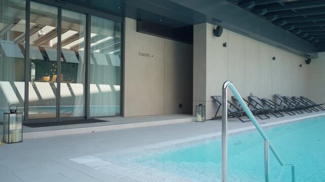 Luxury indoor swimming pool with clear turquoise water in a modern hotel spa. Glass entrance doors and comfortable lounge chairs create a peaceful wellness resort interior for relaxation.
