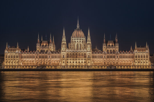 View of the Hungarian Parliament Building illuminated at night, reflecting on the surface of the Danube River in Budapest, Hungary.