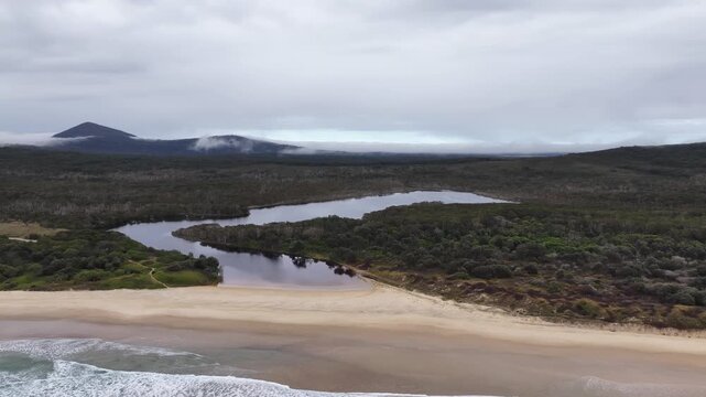 Aerial video flying over the rugged coastline at Lake Arragan, featuring sandy shoreline, rocky formations and waves rolling in from the Pacific Ocean