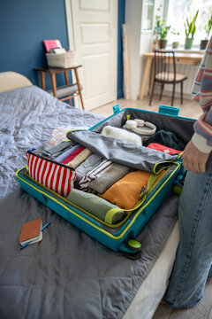 Woman making final checks of neatly packed clothes and essentials in suitcase before holiday trip, personal items and accessories arranged in luggage on bed in bedroom, open travel case with things.