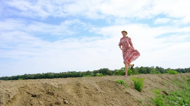 young brunette woman walks along gravel road past lush green bushes and blooming summer wildflowers. Peaceful rural landscape of Croatia offers relaxation and slow living vibes.