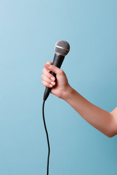 A hand holds a black microphone with a silver grille against a light background.