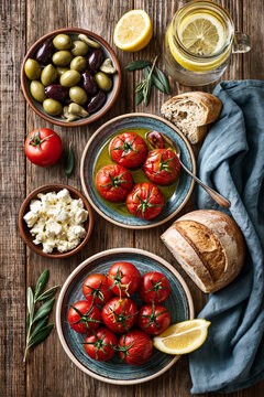 Flat lay shot of a rustic wooden table filled with Mediterranean dishes: green and Kalamata olives, tomatoes with olive oil, feta cheese and bread.