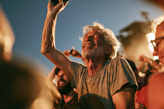 An older music fan in a casual t-shirt standing in the crowd at an outdoor concert or festival, eyes closed in pure joy.