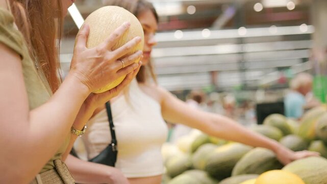 Women choosing ripe melon at supermarket grocery store