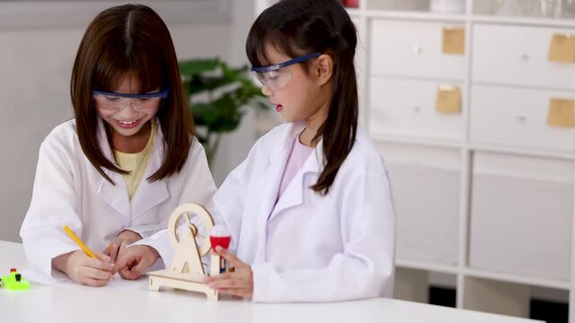 Asian Students in Lab Coats Experimenting with Wooden Wheel Model