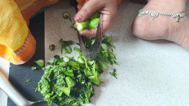 Indian woman chopping fresh ridge gourd vegetable with traditional sickle knife close up