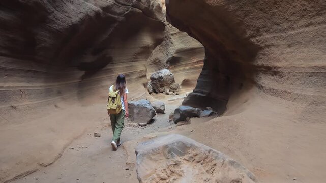 Female hiker with a backpack walking through the narrow passage of the Las Vacas canyon, a unique geological formation in Gran Canaria, Spain