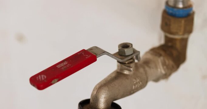 Close-up shot of a human hand turns a red-handled metal valve to switch on a traditional household water pipe using for garden watering.
