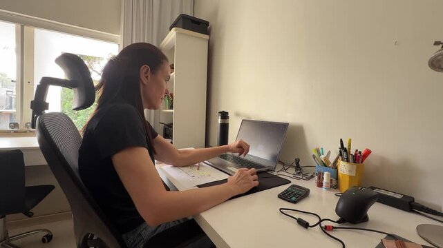 Close-up handheld, dedicated home office workspace with woman focused on her laptop, illustrating remote flexible jobs, digital productivity and modern professional lifestyles