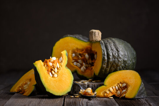 Whole and sliced pumpkin arranged on rustic wooden table with scattered seeds. Autumn harvest still life with squash and seasonal cooking inspiration