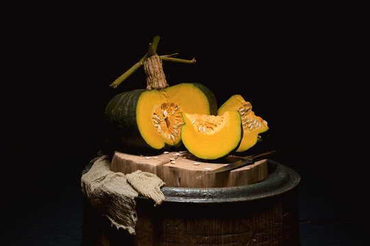 Green pumpkin with cut slices on wooden barrel in low key lighting. Autumn still life with squash and rustic composition