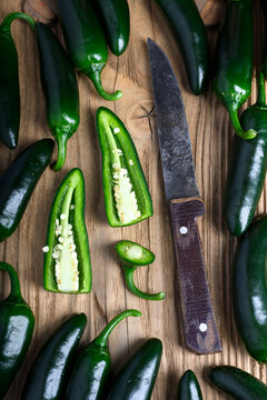 Flat lay jalapeno peppers and slices scattered on wooden surface with knife. Fresh spicy vegetables pattern with organic arrangement