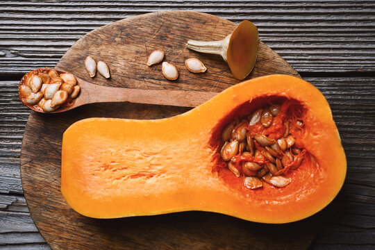 Butternut squash on wooden board with seeds and spoon in rustic setting. Autumn cooking preparation with pumpkin and organic ingredients