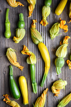 Assorted zucchini with blossoms scattered on rustic wooden background, fresh organic vegetables flat lay, farm harvest concept. Green squash and yellow flowers top view
