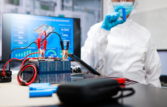 Scientist in protective clothing tests a battery pack with probes and electrical equipment in a modern laboratory, highlighting energy research, safety, and technology.