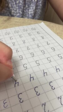 Extreme close up of child hand carefully tracing numbers with pen on practice copybook paper sheet at desk. High quality 4k footage