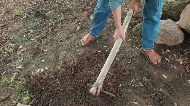 Farmer digging ground and clearing weeds with traditional hoe tool outdoors close up