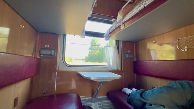 Interior of a sleeper train compartment with berths, seats, table and window. Railway travel scene showing passenger transport, tourism, overnight journey and mobility.
