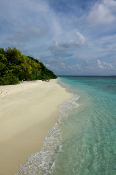 Footprints trail across a deserted white sand beach beside the turquoise sea, Baa Atoll, Soneva Fushi, Maldives