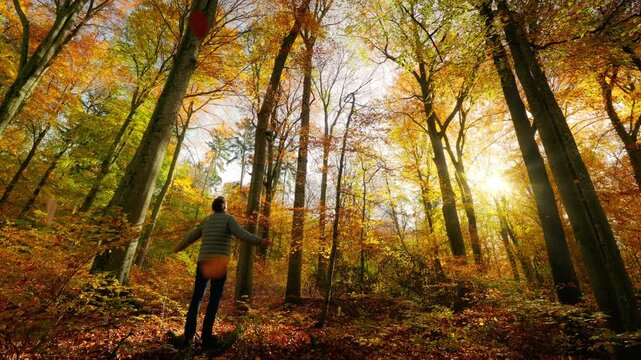 A man standing in a forest, enjoying the autumn sun and taking deep breaths. Connecting with nature on a gorgeous day in the fall season.