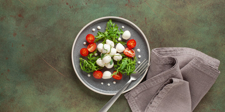 Salad with arugula, mozzarella and tomatoes in a plate on the table. Top view