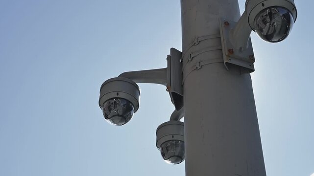 Surveillance cameras are installed on a vertical pole with a clear blue sky in the background. The cameras are positioned to monitor the surroundings, showcasing a modern security feature