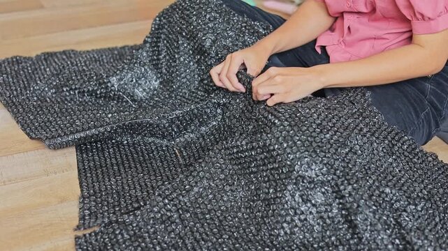 Close-up of hands popping bubbles on sheet of dark plastic bubble wrap packaging at home