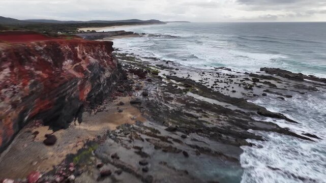 Aerial video flying over the rugged coastline at Lake Arragan, featuring sandy shoreline, rocky formations and waves rolling in from the Pacific Ocean