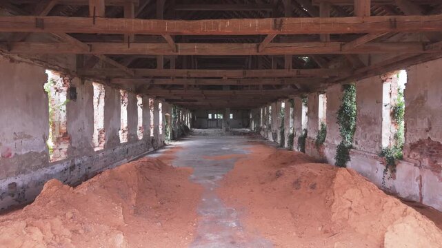 Large open doorway reveals the dark interior of a weathered rural brick building with exposed structural beams, deteriorating walls and piles of loose material on the floor.