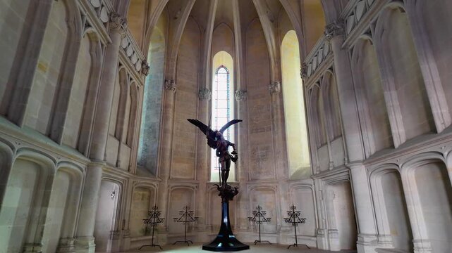 Wide view across the chapel at Ch&acirc;teau de Pierrefonds, centered on a winged Saint Michael sculpture beneath soaring Gothic arches and illuminated stained glass