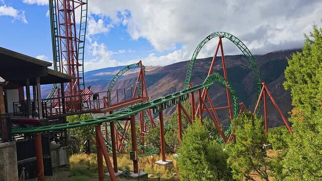 High altitude roller coaster curves over a Rocky Mountain slope near Glenwood Springs, with towering loops, orange supports, forest vegetation, and expansive canyon scenery in daylight.