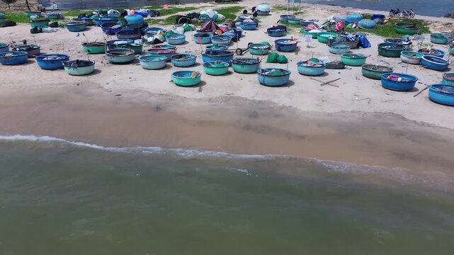 High altitude drone perspective capturing a vibrant pattern of clustered traditional round fishing vessels and basket boats resting on the beach of Mui Ne, Vietnam.