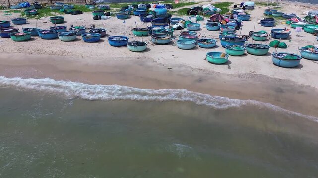 High altitude drone perspective capturing a vibrant pattern of clustered traditional round fishing vessels and basket boats resting on the beach of Mui Ne, Vietnam.