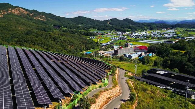 Aerial reveal rising over rows of solar panels on forested hillside above Gunbuk myeon Geumsan South Korea with winding road greenhouses and farm buildings spread across valley below