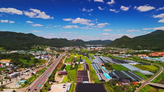 Aerial forward flight along highway above long greenhouse rows and shaded ginseng plots in Geumsan farming village, heading toward valley framed by Maninsan and Seodaesan, South Korea