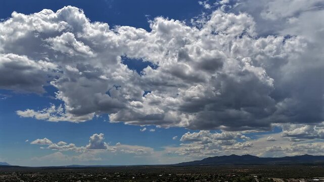 4K drone cloudscape timel apse of a dense sea of afternoon clouds drifting over a serene southwestern landscape. The vibrant blue sky blankets a quiet desert town and distant mountain range.