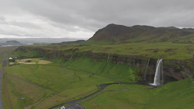 Seljalandsfoss waterfall beneath green cliffs and mountains in southern Iceland, aerial descend