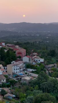 Aerial view of a picturesque traditional Greek village nestled on a lush green hillside during a beautiful sunset in North Corfu, Greece, Mediterranean vacation.