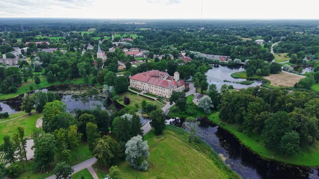Drone nears Dundaga Castle through lush parkland, reflective ponds and village
