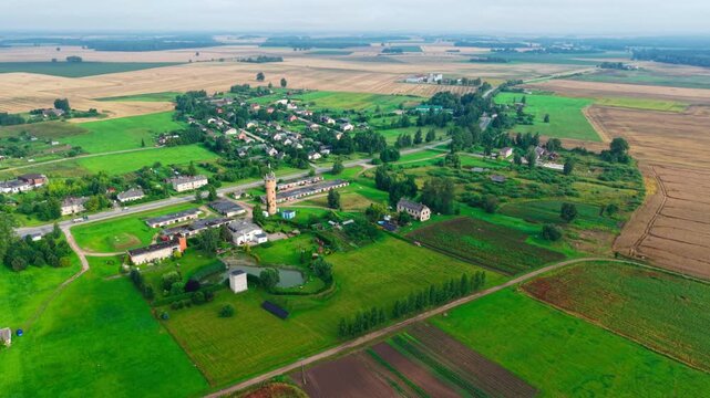Drone pulls away from Jaunberze village revealing green farmland, rural Latvia