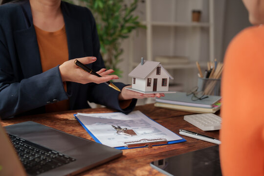 Real estate agent explaining details of a house model to a client, discussing property investment, mortgage, and homeownership during a meeting