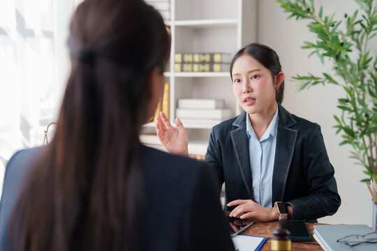 Young Asian female lawyer advising and consulting a client on legal matters, explaining details and answering questions in a professional setting at her desk